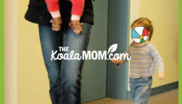Toddler follows mom carrying a baby through a hallway for her playgroup. Photo by Bonnie Way.