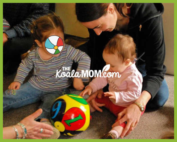 A toddler and a baby play roll-the-ball at a playgroup while mommy watches. Photo by Bonnie Way.
