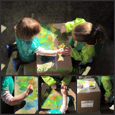 Two little girls painting outside on a box in green smocks.
