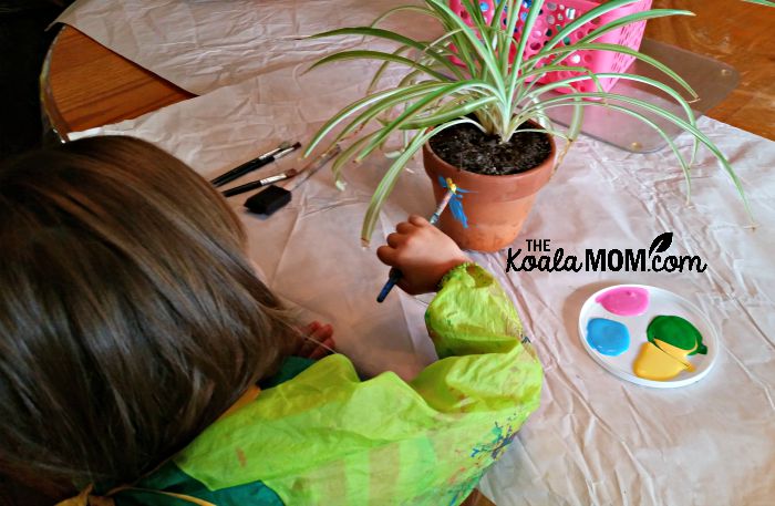 Lily painting her clay plant pot (with spider plant inside)