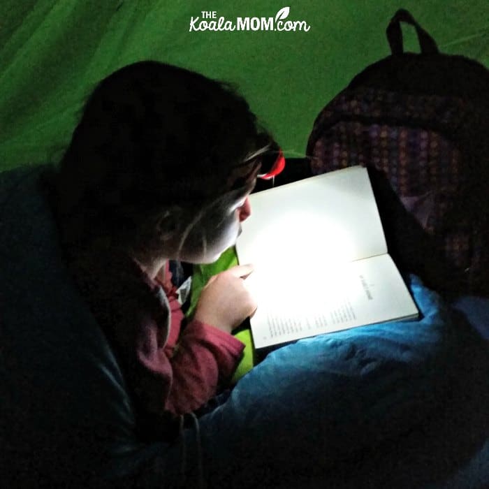 Girl reading a novel in the tent with a headlamp.