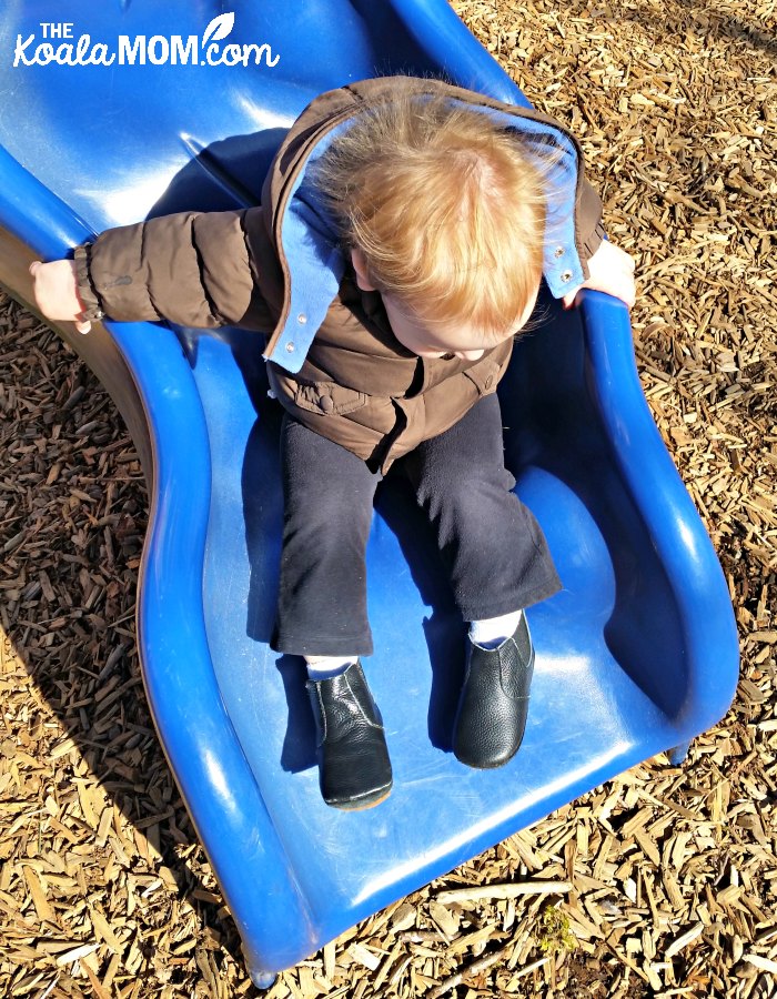 Baby sliding down blue slide with hair getting static.