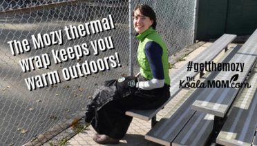 The Mozy thermal wrap keeps you warm outdoors, such as when you're at your child's sporting games like this mom sitting on stadium seating in her Mozy.