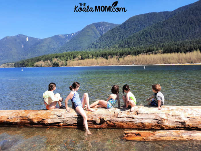 Five kids sitting on a log in Alouette Lake.