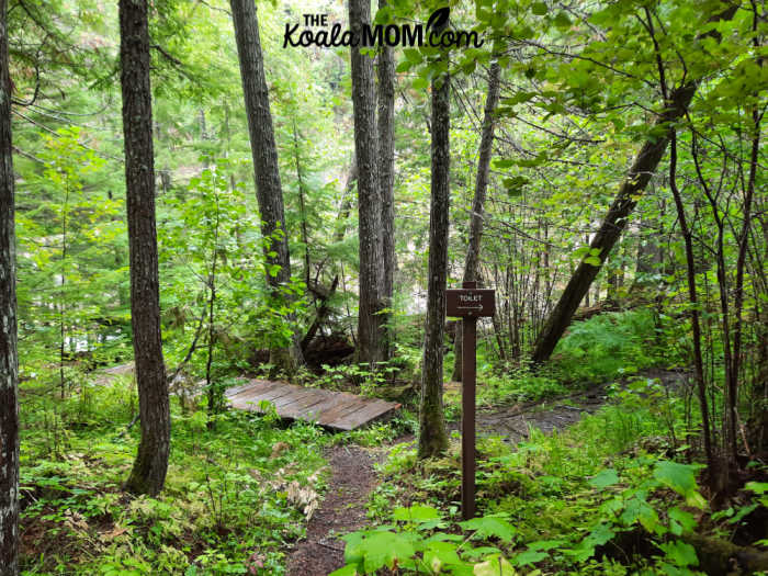 Toilet sign beside a trail with a boardwalk.