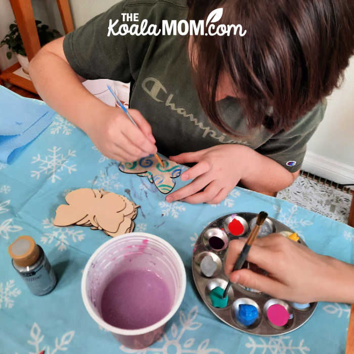 11-year-old paints a wooden butterfly with blue swirls.