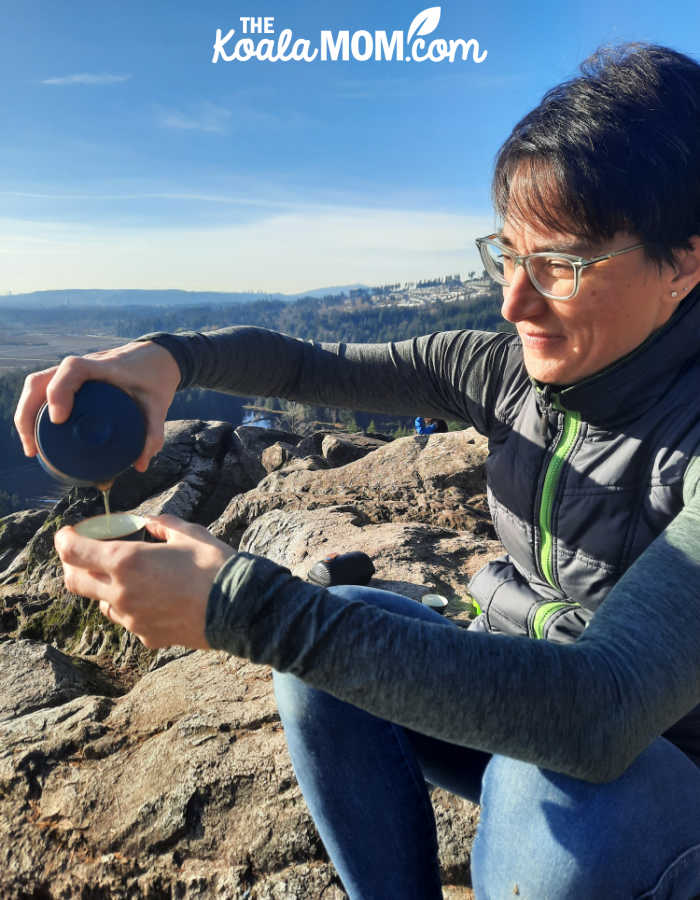 Bonnie pours tea from her Umi travel tea set into her tea cup while sitting on a mountain viewpoint.