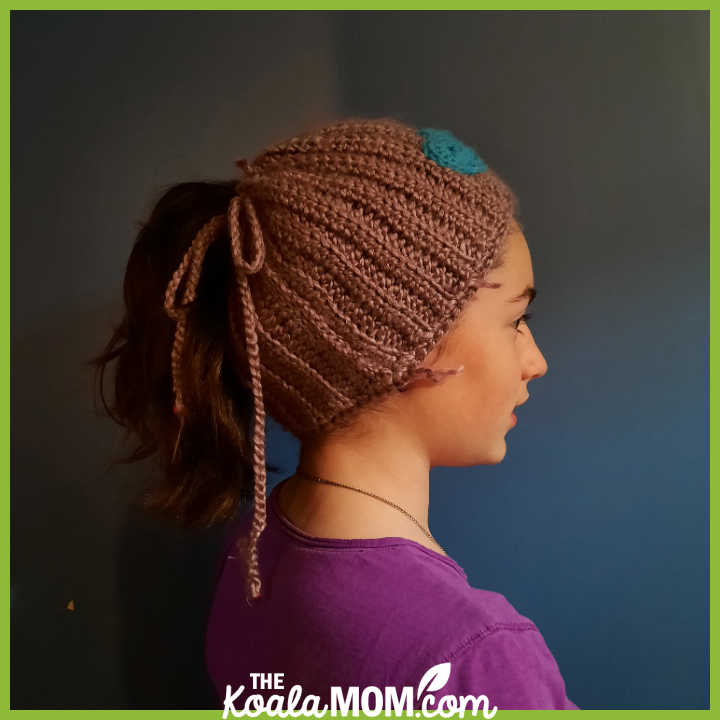 Teenager models her purple DIY crocheted hat, with a high pony tail sticking out of it. Photo by Bonnie Way.