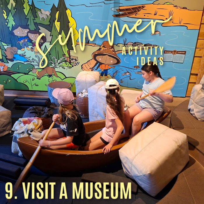 Summer activity ideas 9. visit a museum. Photo of three kids sitting in a wooden boat with a painted mural behind them by Bonnie Way.